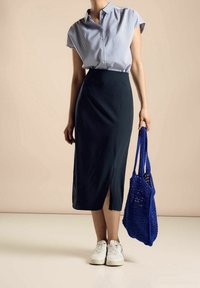 Navy midi skirt with side slit, paired with a striped short-sleeve shirt and white sneakers. Holds a blue knitted tote bag.