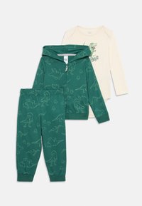 Sudadera con capucha de dinosaurio verde y pantalones a juego, acompañados de una camiseta de manga larga color crema con un gráfico de dinosaurio y texto.