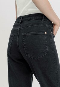 Dunkelgraue Jeans aus Denim verfügen über einen hohen Bund, Gesäßtaschen und subtile Nähdetails. Der Stoff hat eine weiche, lässige Textur.