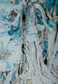 Blumige Blusenstoffe mit hellem Hintergrund und Mustern in Blau, Grau und Beige. Enthält einen Bindeverschluss und ein weiches, strukturiertes Material.
