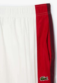 Vyrų šortai balti su raudonomis šoninėmis juostelėmis. Su elastingu juosmeniu ir išsiuvinėtu žaliu logotipu kairėje apatinėje dalyje. Lengvas audinys.