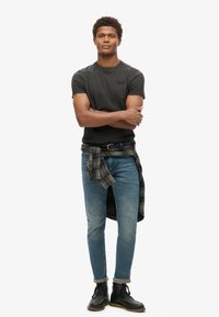 T-shirt nera a maniche corte, jeans slim-fit blu chiaro e stivali neri stringati. Una camicia a quadri verde annodata in vita aggiunge un tocco di dettaglio.