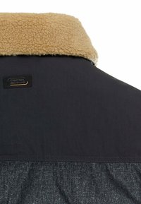 Marine yderjakke med en tan faux shearling krave. Har et Camel Active logo-mærke. Materialet ser glat ud med en subtilt struktureret nederste del.