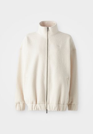Veste zippée en polaire crème, avec un col haut, des poignets côtelés, un ourlet élastique et des poches latérales. Logo discret sur la poitrine.