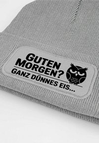 Gray knit beanie with a rectangular patch. Patch displays black text: "GUTEN MORGEN? GANZ DÜNNES EIS" and an owl graphic. Text and design contrast well.
