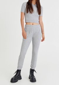 Grauer, cropped, kabelstrick Pullover mit kurzen Ärmeln und Kragen; kombiniert mit grauen Jogginghosen; Modell trägt schwarze, schnürbare Kampfstiefel.
