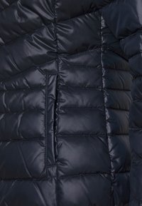 Granatowa pikowana kurtka z przeszyciami, o gładkiej, błyszczącej fakturze i ukośnym wzorze zszycia, z boczną kieszenią.