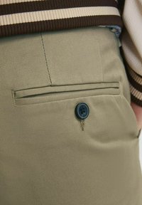 Pantalon vert olive à coupe droite, avec une poche arrière ornée d'un seul bouton noir et un tissu légèrement texturé.