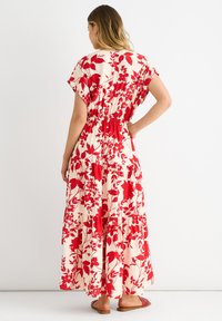 Maxi dress in cream with red floral pattern, short sleeves, elastic waist, and tiered skirt. Worn with flat red sandals.