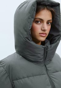 Puffy gray jacket with a large hood, featuring a full zipper and stitched panel details. Smooth texture with a matte finish.