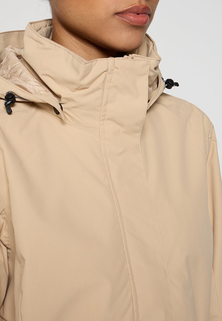Beige wasserdichte Jacke mit hohem Kragen, verstellbaren Zugbändern und glatter Textur, ausgestattet mit einem Frontreißverschluss und Nahtdetails.