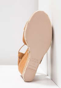 Sandale compensée en daim beige avec semelle en jute style espadrille, semelle en caoutchouc et bride à la cheville, montrant la semelle inférieure avec les détails de la marque et de la taille.