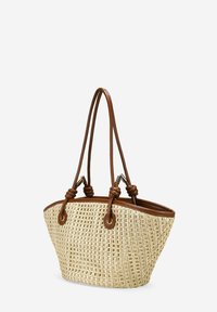 Bolso de tote de paja trenzada con un ribete y asas de cuero sintético marrón. Presenta una forma triangular y un patrón texturizado notable en el cuerpo.