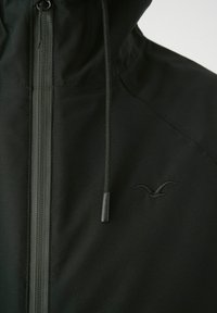 Schwarze Reißverschlussjacke mit einer Kordelzugkapuze und einem dezenten Logo. Der Stoff hat eine glatte, matte Textur mit gesteppten Nähten.