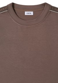 Hnědé tričko s krátkými rukávy z měkké, hladké látky. Má kulatý výstřih a kontrastní štítek podél ramen.