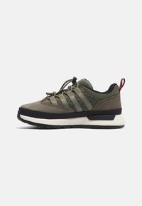 Zapatillas deportivas en verde oscuro con una parte superior de tela texturizada, cordones elásticos y suela de goma negra. Presentan un acento rojo en el talón.