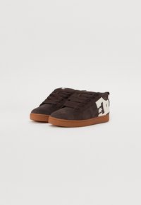 Braune Wildledersneaker mit Gummisohle, ausgestattet mit einem cremefarbenen Logo an der Seite und strukturierten Schnürsenkeln. Rundliche Zehenform und gepolsterter Kragen.