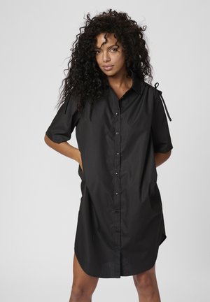 Vestito camicia nero con maniche corte, colletto e tasche laterali. Presenta lacci sulle spalle e un orlo leggermente curvo.