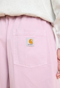 Pink cotton pants featuring a back pocket with a Carhartt logo patch. The fabric has a smooth texture and a slightly relaxed fit.