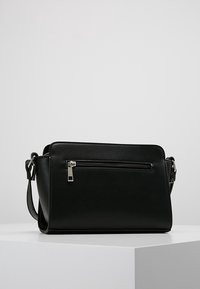 Sort crossbody taske lavet af glat læder, med en lynlåslomme foran, justerbar rem og slank rektangulær form.