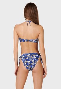 Completo bikini blu con motivo astratto bianco. Si annoda al collo e ai fianchi, con un top strutturato e un design a copertura minima per il fondo.