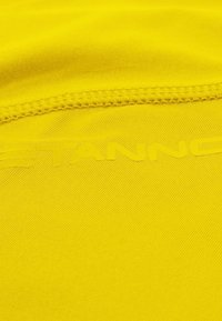 Tela de color amarillo brillante con una textura suave, que presenta costuras tonales y un logo en relieve en amarillo más claro en el centro.