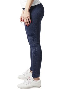 Mornarsko plave rastezljive tajice s rebrastim detaljima na bokovima, visokim strukom i glatkom, denim-texturom. Nosi se s bijelim tenisicama.