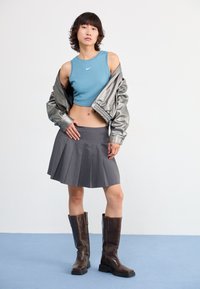 Gray pleated skirt paired with a blue crop top and a metallic silver bomber jacket. Brown knee-high boots complete the outfit.