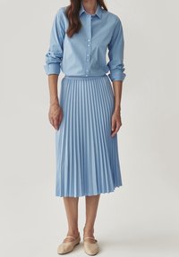 Camicia button-up azzurro chiaro abbinata a una gonna plissettata azzurro chiaro. L'outfit presenta un tessuto morbido e un design classico con una vita attillata.