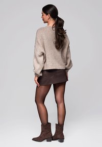Beige pletený svetr, mini sukně z hnědé kůže, průhledné punčochy a hnědé semišové kotníkové boty. Vymezený tvar s žebrovanou strukturou a mírně nafouklými rukávy.