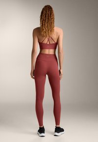 Vínový športový podprsenka s prekríženými ramienkami a legíny s vysokým pásom. Hladká textúra, priliehavý strih, doplnené čiernymi športovými topánkami.