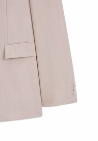 Manche et bas avant de veste beige clair ajustée, avec quatre boutons blancs sur le poignet et une poche à rabat horizontale.
