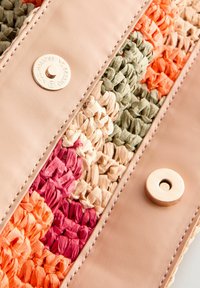 Sac en paille tissé avec des sections en orange, rose, vert et beige, doté d'une bande en cuir rose et d'une fermeture à pression en or. Fini texturé.
