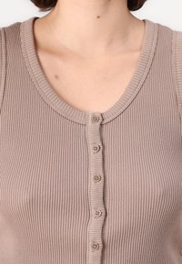 Tricou fără mâneci de culoare maro, cu decolteu rotund și o linie de șase butoane asortate pe partea din față; textură de țesătură moale.