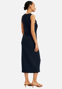 Marineblaues, geripptes Midi-Kleid mit ärmellosem Design, figurbetonter Form, Seitenschlitzen und einer dezenten Textur. Kombiniert mit hellbraunen, hohen Sandalen.