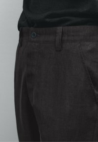 Tummanharmaat housut, jotka on valmistettu teksturoidusta kankaasta. Klassinen malli, jossa on nappikiinnitys ja hillityt sivutaskut.