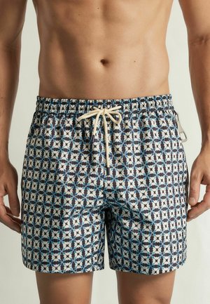 Mann trägt blaue, weiße und schwarze Badehose mit geometrischem Muster, elastischem Bund und Kordelzug.