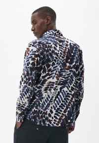 Camisa de manga larga en blanco con un patrón abstracto multicolor que presenta tonos de azul marino, marrón y negro. Cuello estándar, diseño de corte recto.