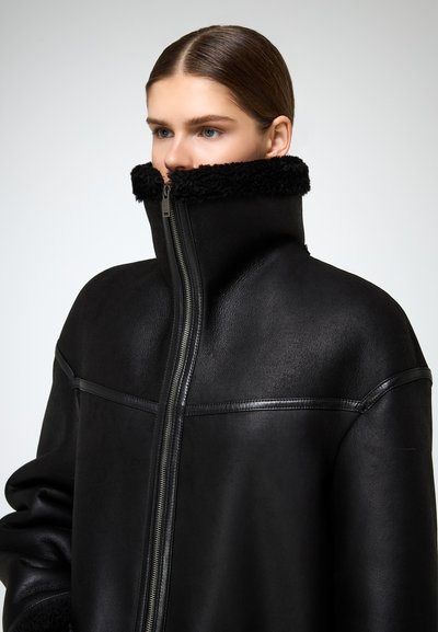 Crna kožna jakna s visokim ovratnikom s plišanim oblogom, prednjim zatvaračem i glatkom teksturom, osmišljena za suvremen izgled.