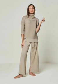 Beige Strickpullover mit hohem Kragen und kurzen Ärmeln, kombiniert mit weiten beigen Hosen, die seitliche Schlitze und eine gebundene Akzentuierung an der Taille haben.