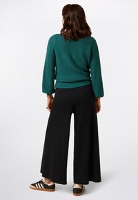 Teal knitted sweater with loose, textured weave and long sleeves, paired with wide black trousers and black/brown sneakers.