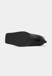 Calzature nere con una tomaia liscia e una suola strutturata. Il design presenta una punta affusolata e un piccolo tacco accentato sul retro.