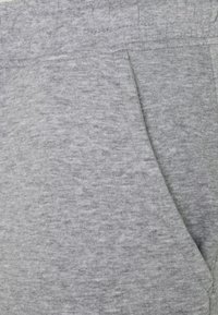 Chándales de tela gris que presentan una textura suave, cinturilla elástica y un bolsillo lateral con un sutil patrón jaspeado creado por tonos variados.