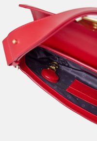 Borsa a mano in pelle rossa con una texture liscia, accessori dorati e un rivestimento interno scuro a motivi che presenta un portachiavi rotondo.