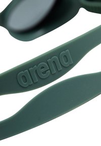 Las gafas de natación de silicona verdes cuentan con una correa texturizada con el logotipo "arena" y lentes oscuros redondeados para su uso en la natación.