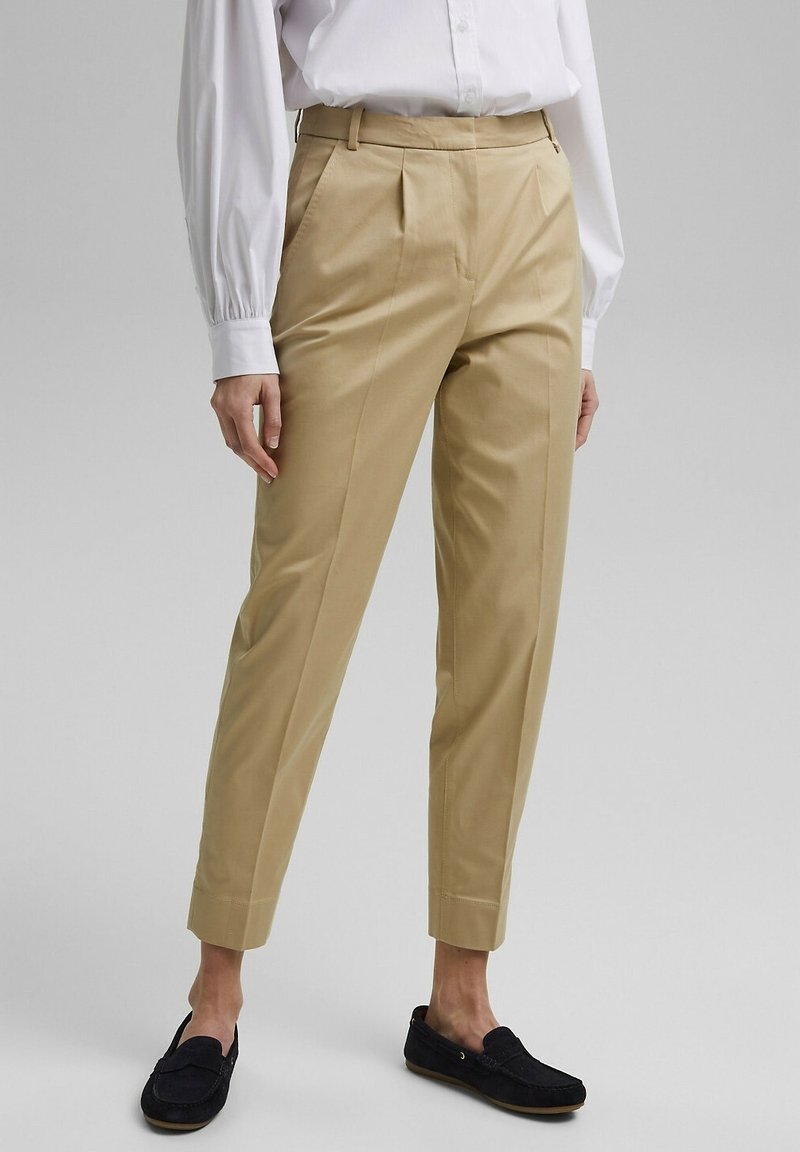 Pantaloni beige su misura con gamba dritta e dettagli delle pieghe. Realizzati in tessuto liscio, presentano un frontale piatto e tasche laterali, abbinati a mocassini blu navy.