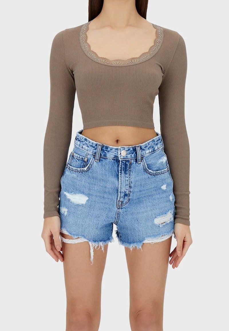 Bruin ribgebreid cropped shirt met lange mouwen en kanten rand, gecombineerd met beschadigde denim shorts met rafelige zoom en verschillende blauwtinten.