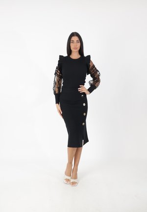 Top negro con canalé y detalles de volantes en los hombros, mangas abullonadas transparents y una falda midi negra ajustada con una abertura lateral y botones decorativos.