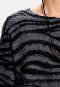 Pull-over gris à rayures zèbre noires, fabriqué en matière douce et duveteuse. Présente un large col et des détails texturés.