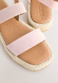 Sandales en daim rose avec deux larges brides, une semelle intérieure douce couleur noisette, et un talon compensé en jute tressé pour plus de hauteur et de texture.